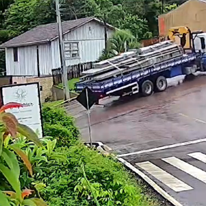 Caminhão carregado de postes de concreto derrapa e atinge casa